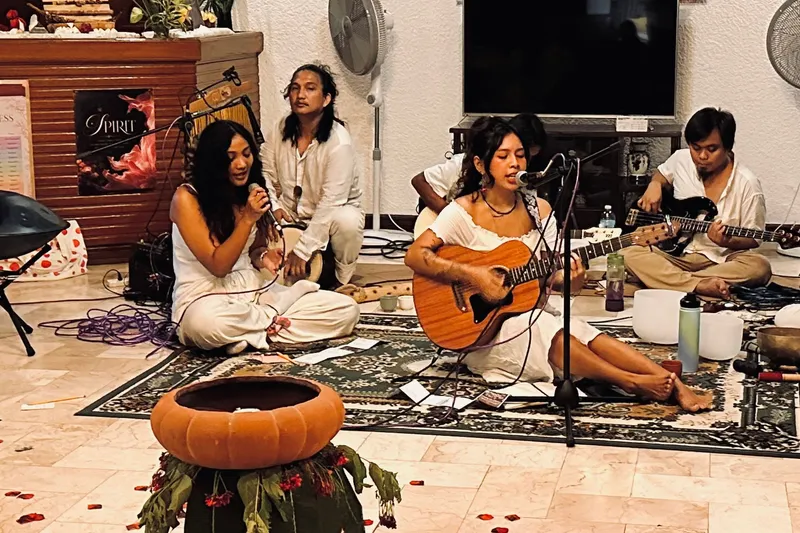 Musicians in white seated before the Tallaro banner with a clay cacao vessel, petals, and candles in the foreground