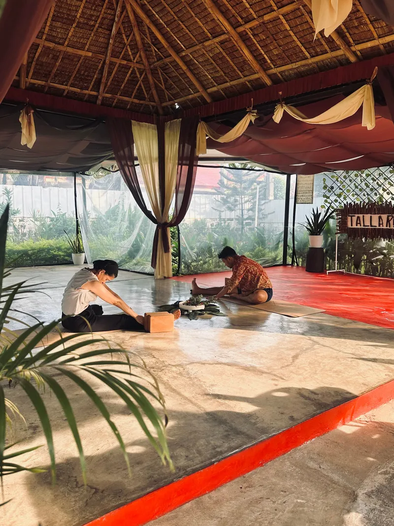 A private outdoor yoga session with a Tallaro teacher guiding a student through a seated twist on mats under open sky