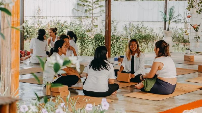 Women in white tops sitting on cork mats in a circle at Tallaro, one smiling with a yoga block and white flowers in front